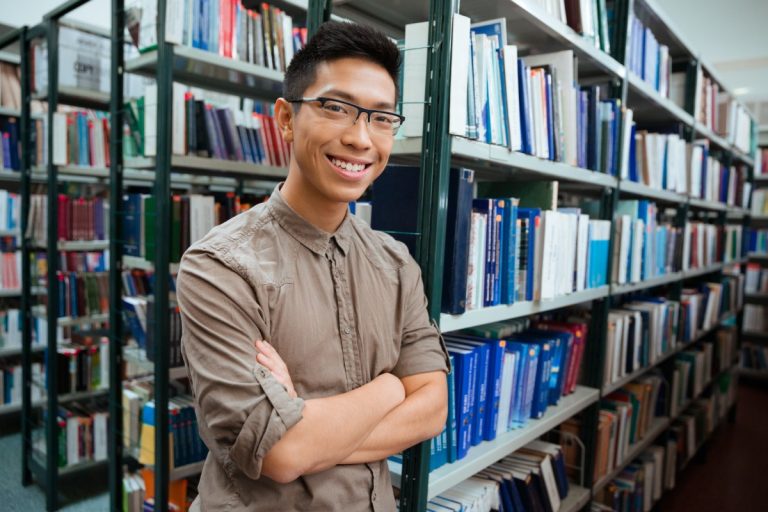 Man standing with arms folded in university library